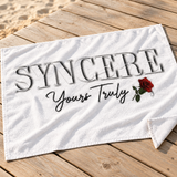 Close-up of SYNCERE Yours Truly lettering and red rose on a white towel on a wooden deck